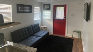 A living room with a dark sofa, a small round table, a red door, and a mounted TV.