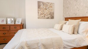 A neatly made bed with a quilted cover, a wooden headboard, and a wall with a floral wallpaper. - 3 Mill Wynd (Darlington)