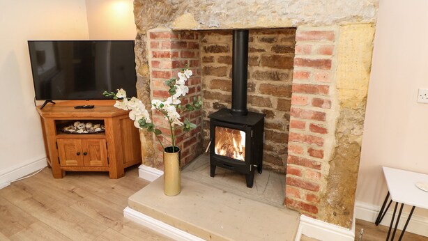 A living room with a stone fireplace, a television on a wooden stand, and a vase with white flowers. - 3 Mill Wynd (Darlington)