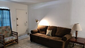 Een woonkamer met een bruine bank, een houten stoel, een lamp en een deur.