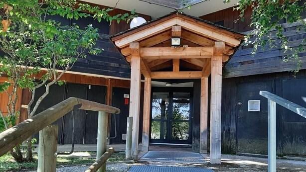 En entré av trä med en överbyggd veranda som leder till en byggnad med en svart dörr.