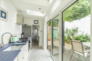 A modern kitchen with a gas stove, a toaster, and a sink. There is a hallway leading to a glass door opening to a garden. - 9 St John's Street - a family break that sleeps 6 guests in 3 bedrooms (York)