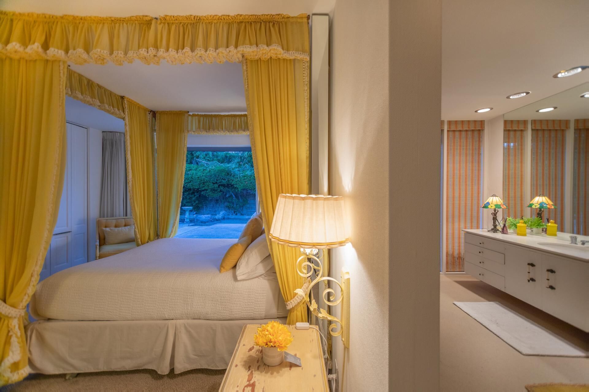 Una camera da letto con un letto grande, tende gialle, una lampada da comodino e vista sul verde.