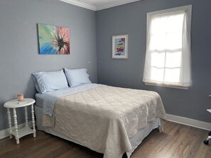 Une chambre à coucher comprenant un lit, une petite table de chevet, une fenêtre et deux œuvres d’art murales.