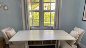 A dining table with four chairs, a window with curtains, and a view of greenery outside. - Historic Cottage  (Delray Beach)