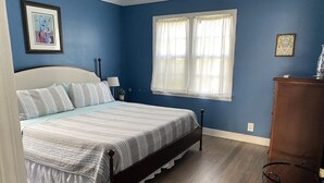 A bedroom with a bed, a window with curtains, a dresser, and a nightstand. - Historic Cottage  (Delray Beach)