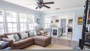 A living room with a brown sectional sofa, a ceiling fan, and large windows. - Historic Cottage  (Delray Beach)