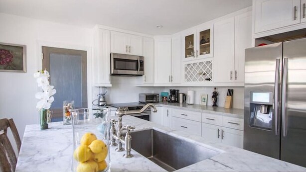 A modern kitchen with white cabinetry, stainless steel appliances, and a marble countertop. - Historic Cottage  (Delray Beach)