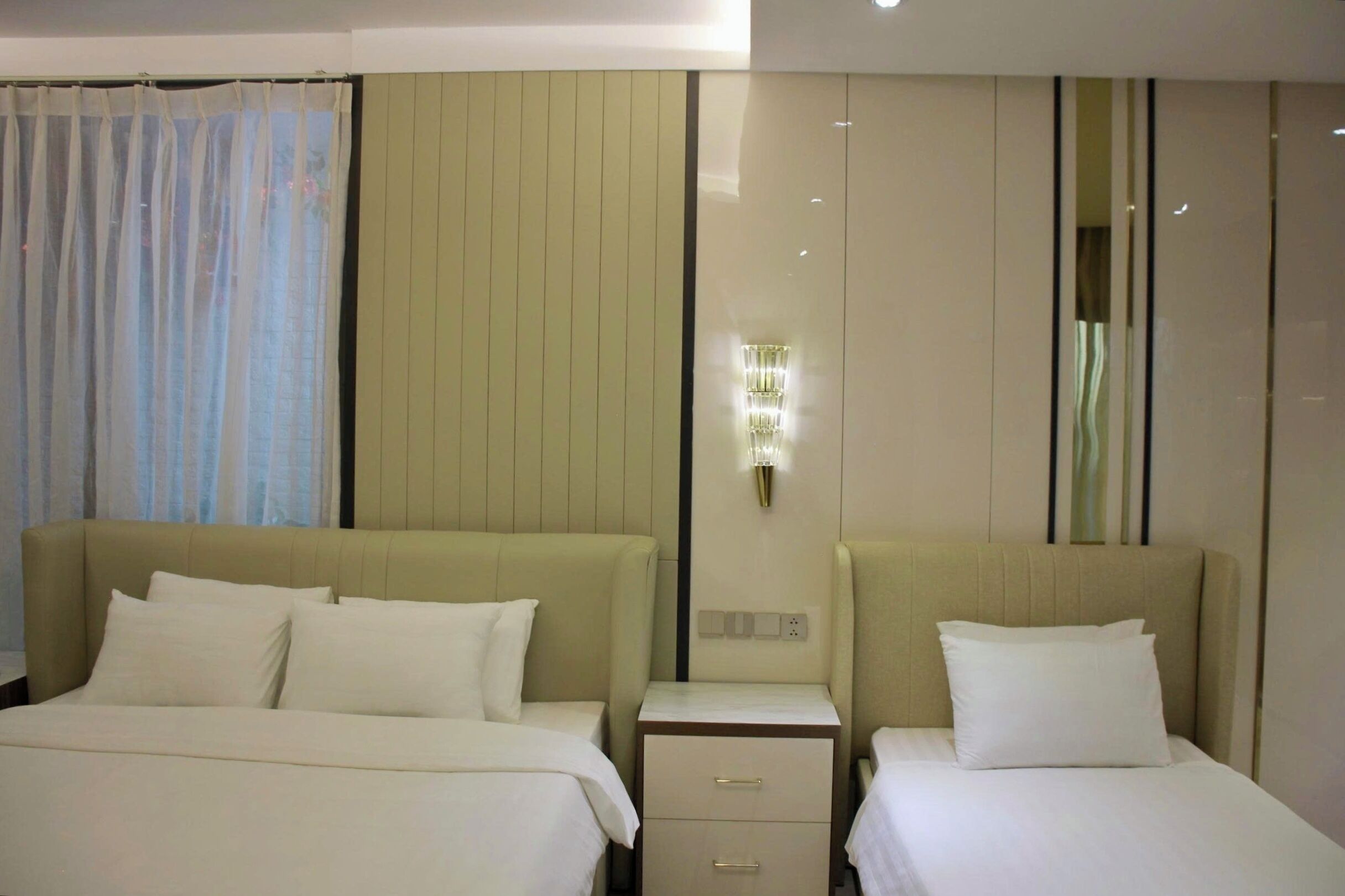 A hotel room with two beds, a nightstand with drawers, a wall-mounted light fixture, and a mirror.