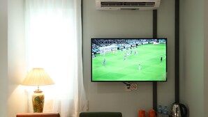 Un téléviseur fixé au mur diffusant un match de football, une lampe, une chaise et une table avec des tasses et une bouilloire.