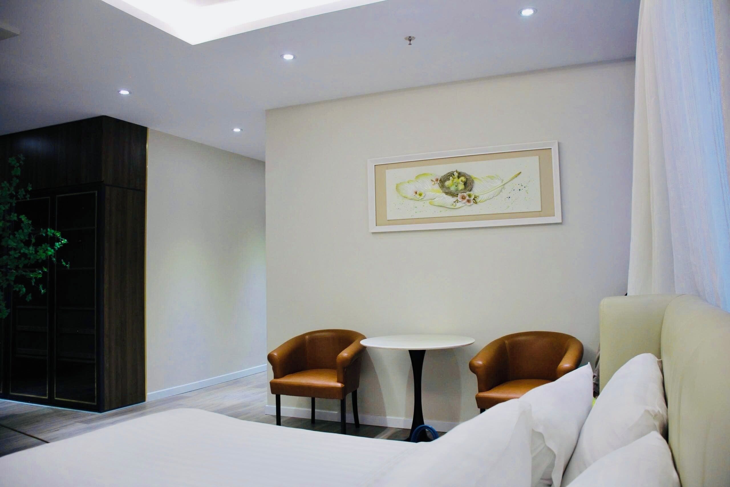 Een moderne hotelkamer met een bed, twee bruine fauteuils, een klein rond tafeltje en een kunstwerk in een lijst aan de muur.