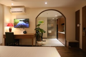 A hotel room with a bed, desk, TV, potted plant, and a view of the hallway. - Lanura Apartments and Hotel (Ho Chi Minh City)