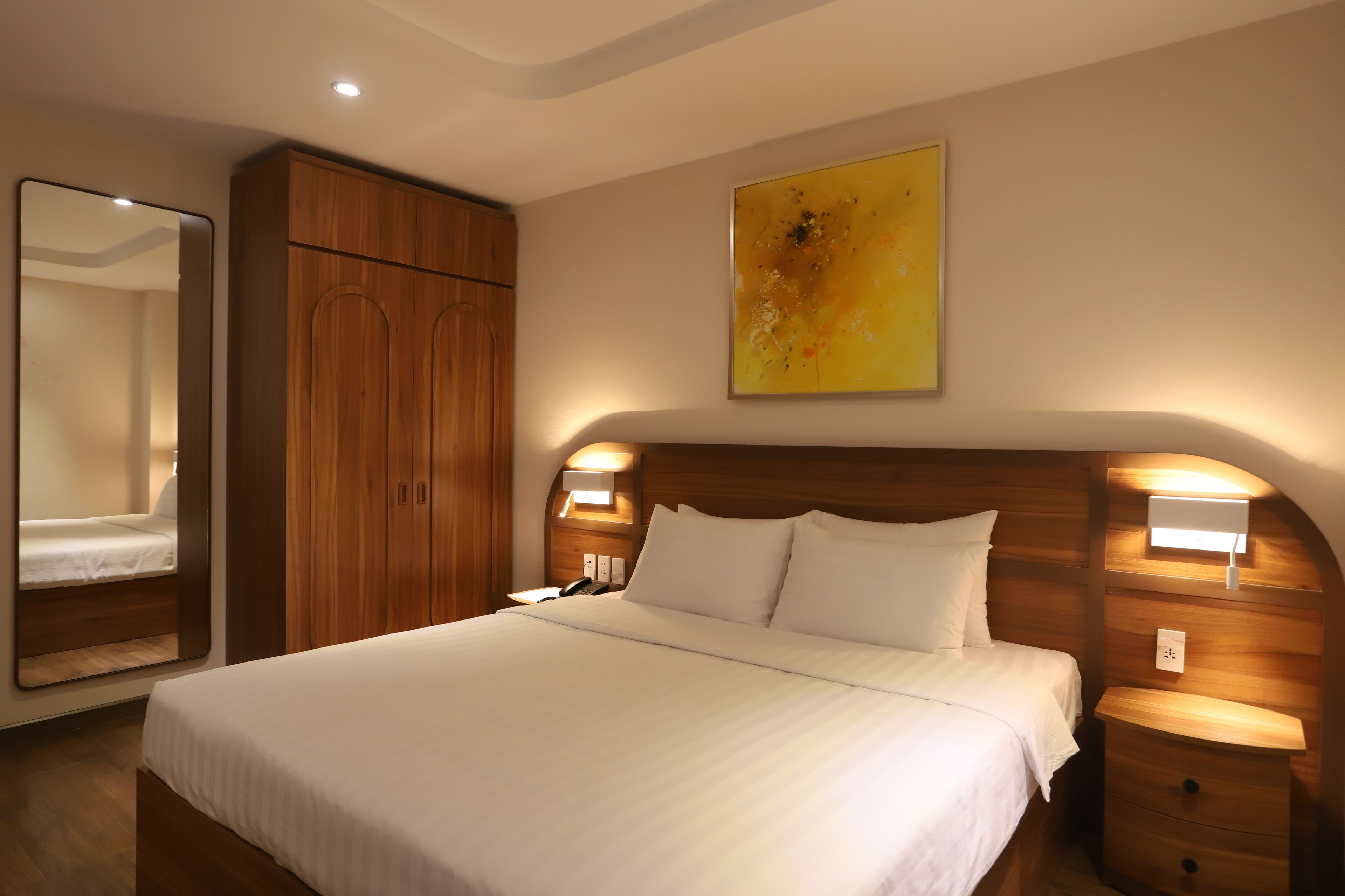 Una habitación de hotel con una cama grande, un armario de madera, lámparas de noche y un cuadro en la pared.