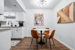 Uma cozinha moderna com armários brancos, uma mesa de jantar redonda com quatro cadeiras e um lustre.