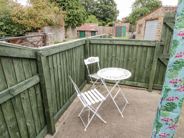A wooden fence, a white folding chair, and a small round table in a backyard. - Ducky's (Pickering)