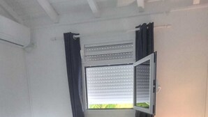 A bedroom with a bed, a window with blinds, a nightstand with a lamp, and a small table with a lamp.
