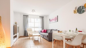 A modern living room with a sofa, dining table, and chairs. There is a TV and a lamp in the corner. - High quality apartment 1 bedroom, 1 bathroom La Algaba (Algaba)