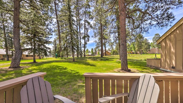 A deck with Adirondack chairs overlooking a grassy area with trees and a building in the background. - Cozy Pagosa Springs Townhome w/ Patio! (Pagosa Springs)