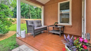 Eine überdachte Veranda mit einem Korbsessel, einem kleinen Tisch und einem Blumentopf.