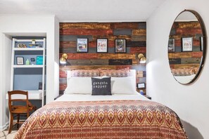 Une chambre à coucher comprenant un lit, une tête de lit en bois, un miroir, une chaise et une étagère avec des livres et des objets décoratifs.