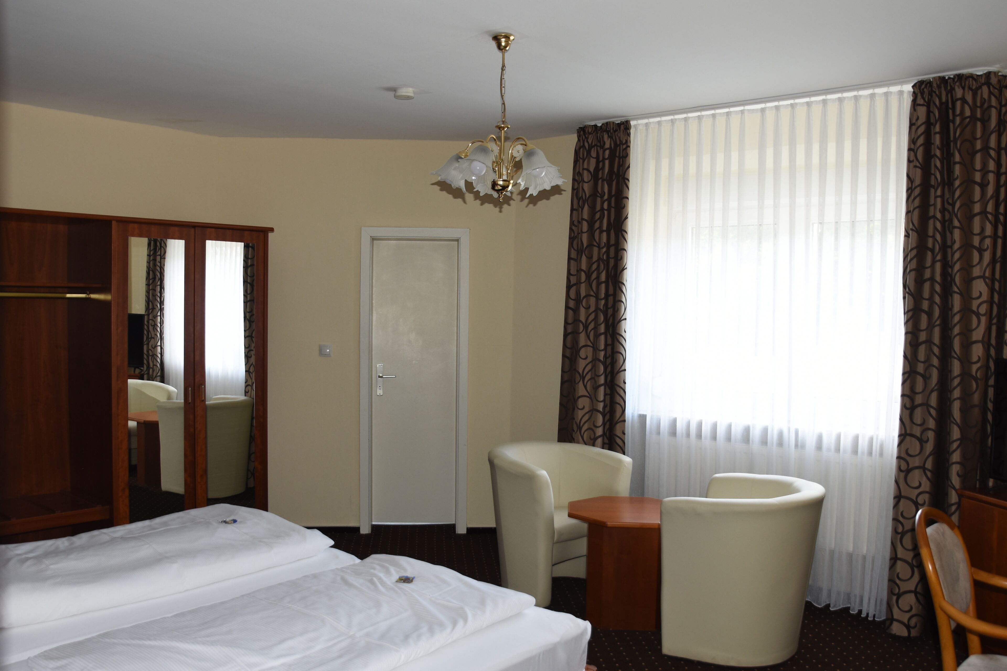 A hotel room with a large bed, two armchairs, a small table, a mirror, and a door.
