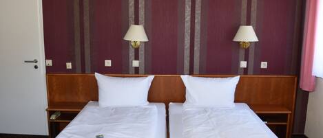 A hotel room with two single beds, wooden headboards, white linens, two bedside lamps, and a striped wall.