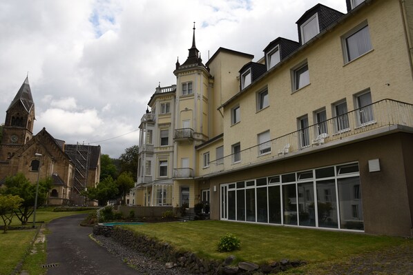 A historic building with a tower, adjacent modern buildings, and a paved pathway. -  Trip Inn Parkhotel Bad Ems (Bad Ems)