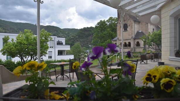 Une terrasse extérieure avec des tables et des chaises, entourée de plantes et de fleurs en pot.