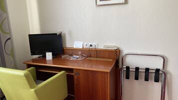 Ein Hotelzimmer mit einem Holztisch, einem Computer, einem Stuhl, einem Telefon und einer Heizung.
