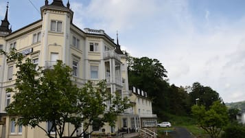 Un grand hôtel historique, doté d’une tour et d’un balcon imposants, entouré d’une végétation luxuriante et d’un jardin bien entretenu.