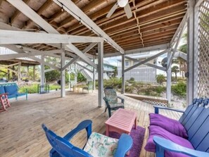 Un espacio al aire libre techado con piso de madera, mobiliario azul y morado, y vistas del paisaje circundante.