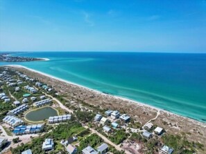 An aerial view of a coastal resort with multiple bungalow-style accommodations, a sandy beach, and a clear blue sea.
