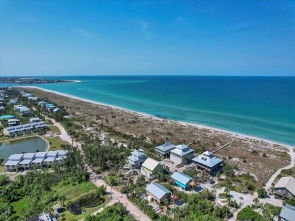 Vista aérea de un complejo turístico costero con varios edificios, una playa y un lago pequeño.