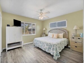 A bedroom with a bed, a ceiling fan, a window with blinds, a nightstand, and a cabinet.
