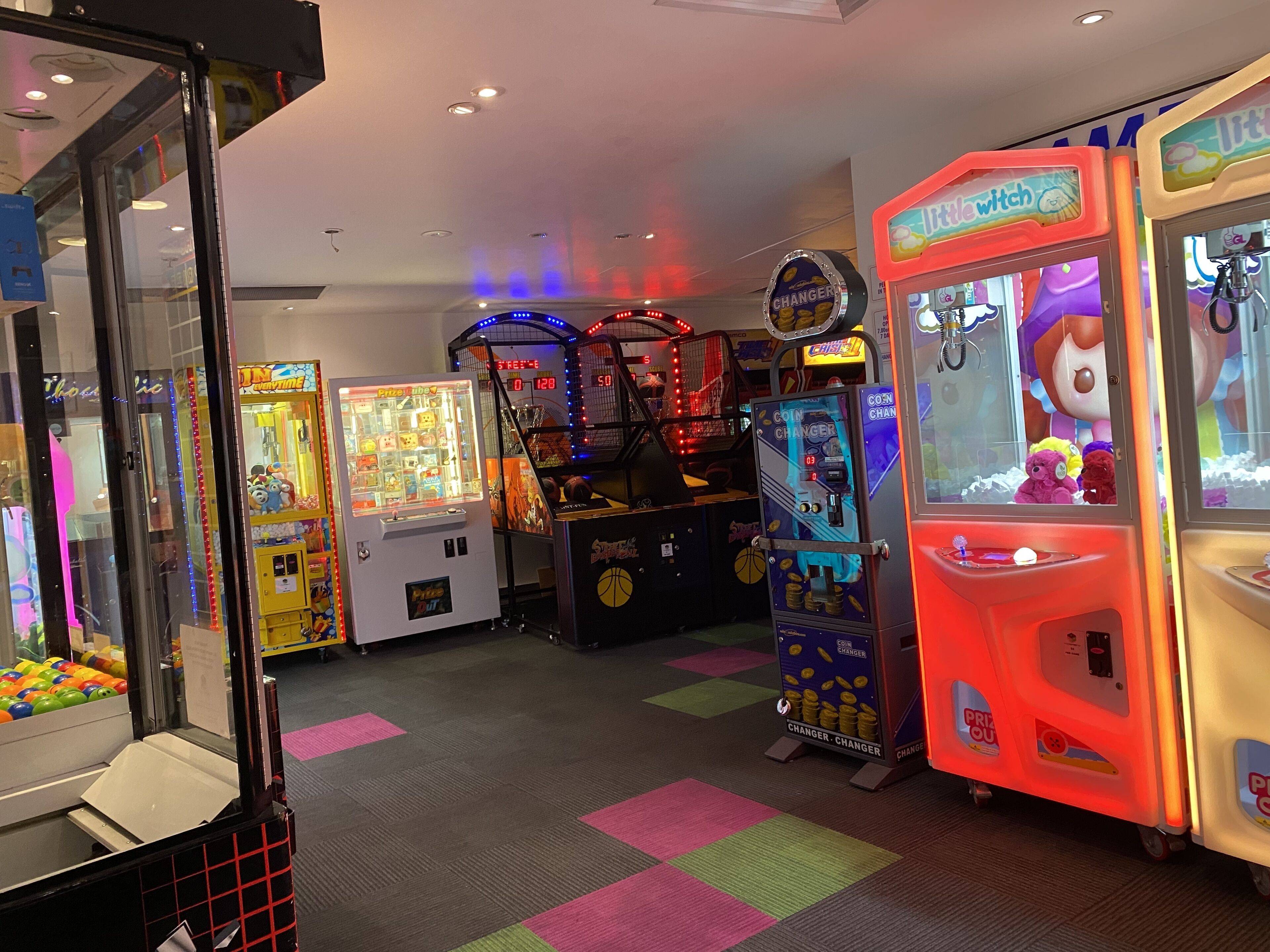 A variety of arcade games in a brightly lit indoor space with colorful floor tiles.