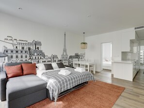 Quarto moderno com mural da paisagem urbana, sofá cinza, cama com manta listrada e um pequeno espaço de refeições.