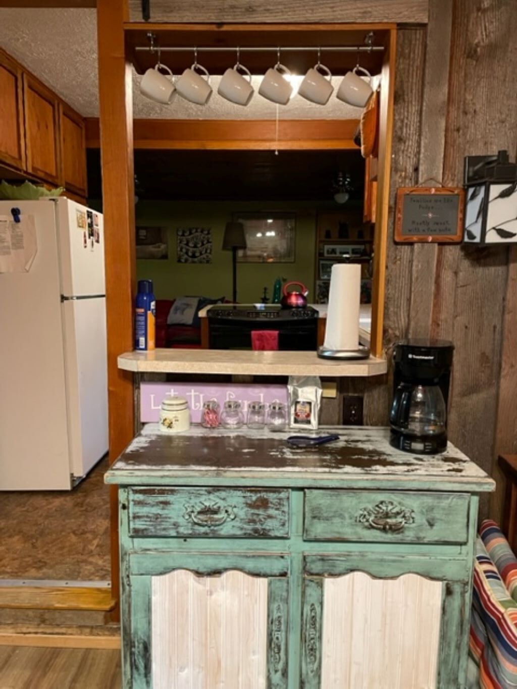 A kitchen with a rustic wooden cabinet, a coffee maker, and a refrigerator.