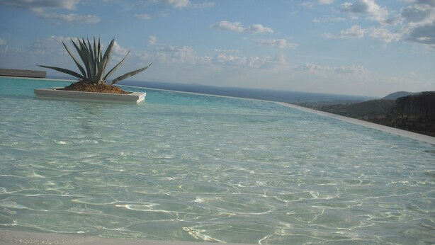 A clear pool with a plant in the center, surrounded by a clear sky and distant mountains. - Masseria del Piano (Campofelice di Roccella)
