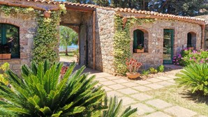 A stone building with arched doorways and windows, surrounded by lush greenery and potted plants. - Masseria del Piano (Campofelice di Roccella)