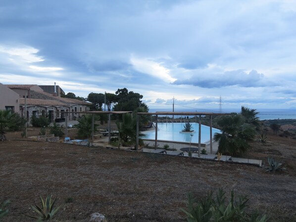 A swimming pool with a pergola, surrounded by palm trees and a view of the sea. - Masseria del Piano (Campofelice di Roccella)