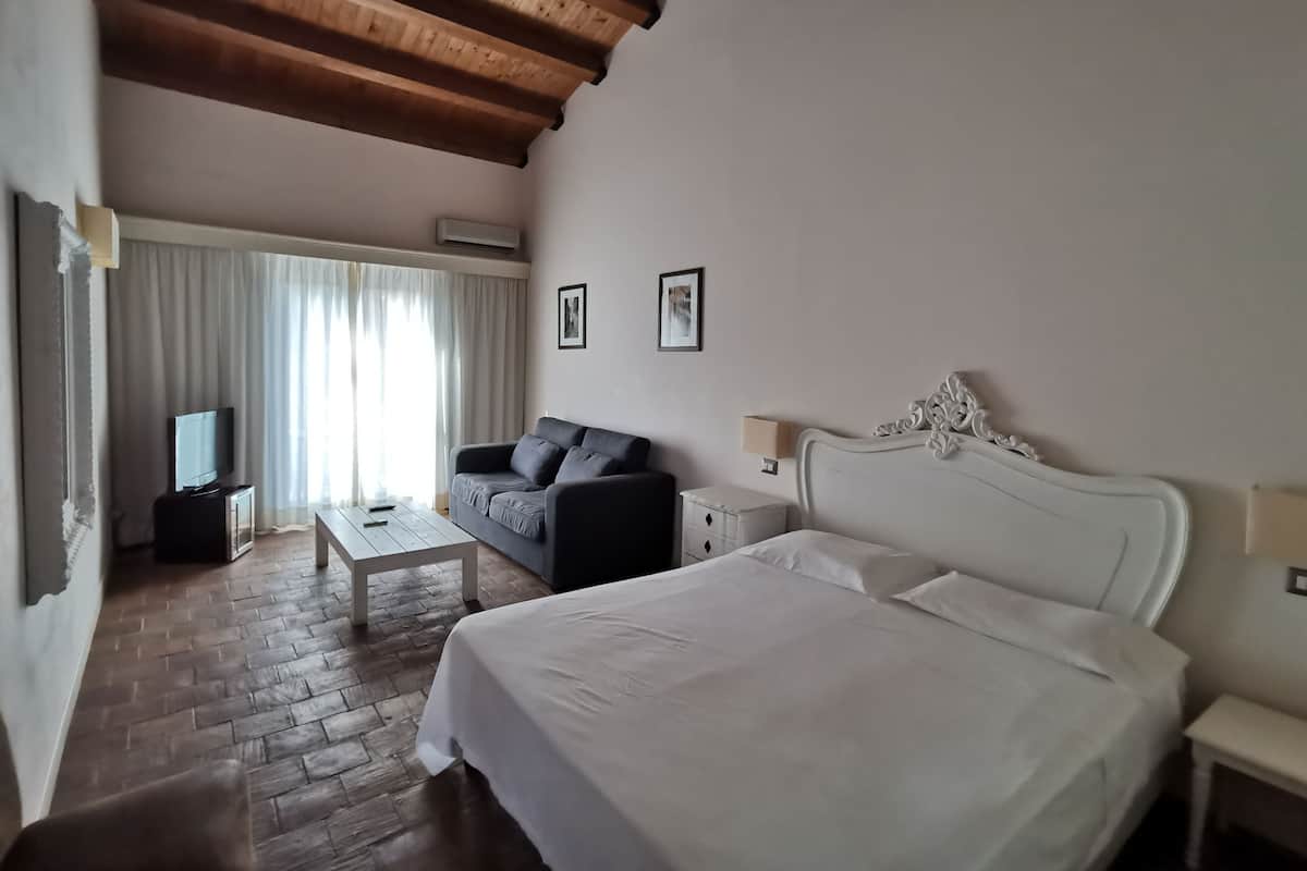 A hotel room with a large bed, a sofa, a TV, and a wooden ceiling.