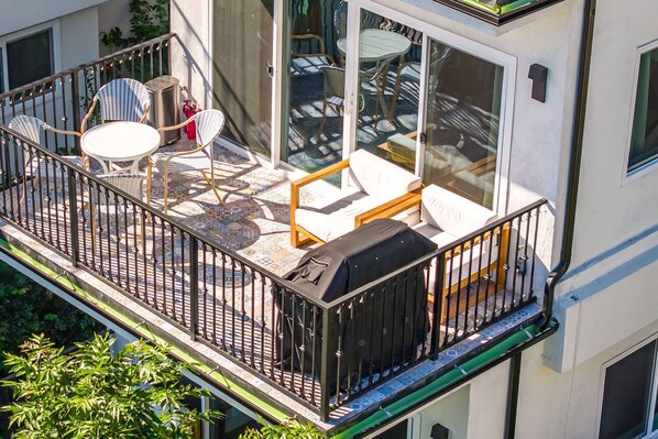 A balcony with outdoor furniture, a grill, and a view of the street.