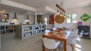 Eine geräumige Küche mit Holztisch und weißen Stühlen, einer hängenden Leuchte und einem großen Korbwannenkorb.