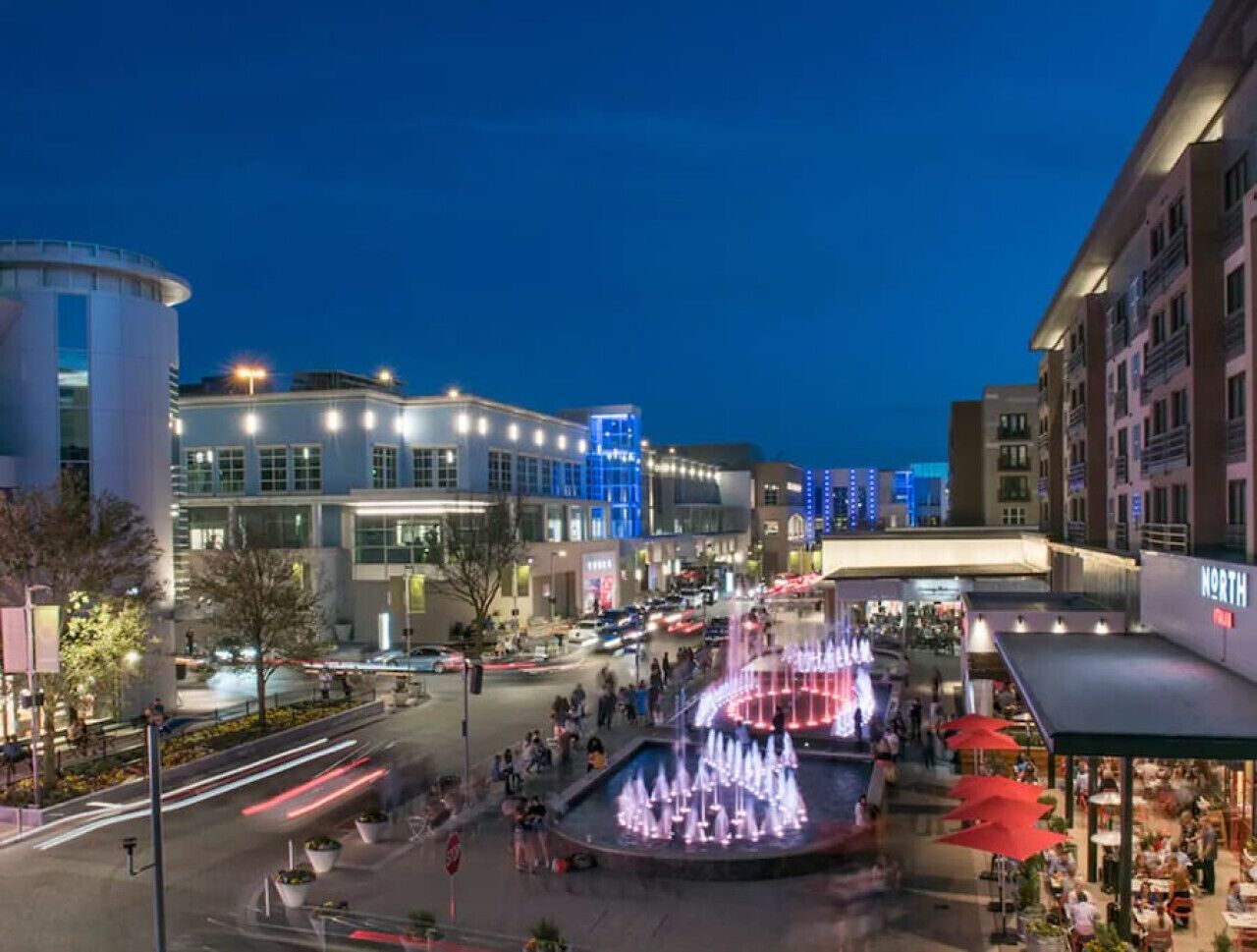 A public square with a fountain, surrounded by modern buildings and outdoor seating areas.