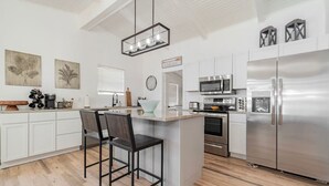 A modern kitchen with white cabinets, stainless steel appliances, and a central island with bar stools. - Remodeled Lakefront! Private beach, toys & hot tub (Little Elm)