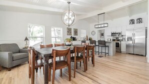 A modern kitchen with a dining area, featuring a wooden table and chairs, a sofa, and a large window providing natural light. - Remodeled Lakefront! Private beach, toys & hot tub (Little Elm)