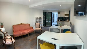 A compact living space with a sofa, chairs, a dining table, and a TV mounted on the wall. - Appartement AU Coeur DU Pays Basque (Urrugne)