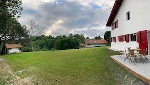 A house with a patio area featuring a table and chairs, surrounded by a well-maintained lawn and trees. - Appartement AU Coeur DU Pays Basque (Urrugne)