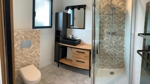 A bathroom with a toilet, a sink with a mirror, a shower, and a cabinet. - Appartement AU Coeur DU Pays Basque (Urrugne)