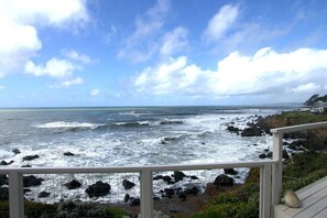 A coastal view with waves crashing against rocks, a clear sky, and a wooden deck.
